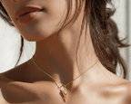 Close-up of a woman wearing a gold necklace with a diamond pendant against a neutral background