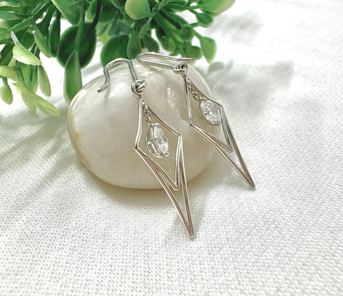 Silver earrings with lab grown diamonds on a white fabric background with green leaves.