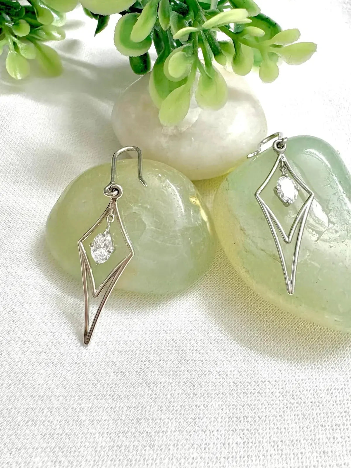 Silver earrings with lab grown diamonds on a light background with greenery