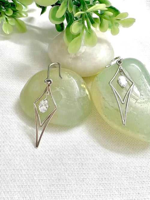 Silver earrings with lab grown diamonds on a light background with greenery